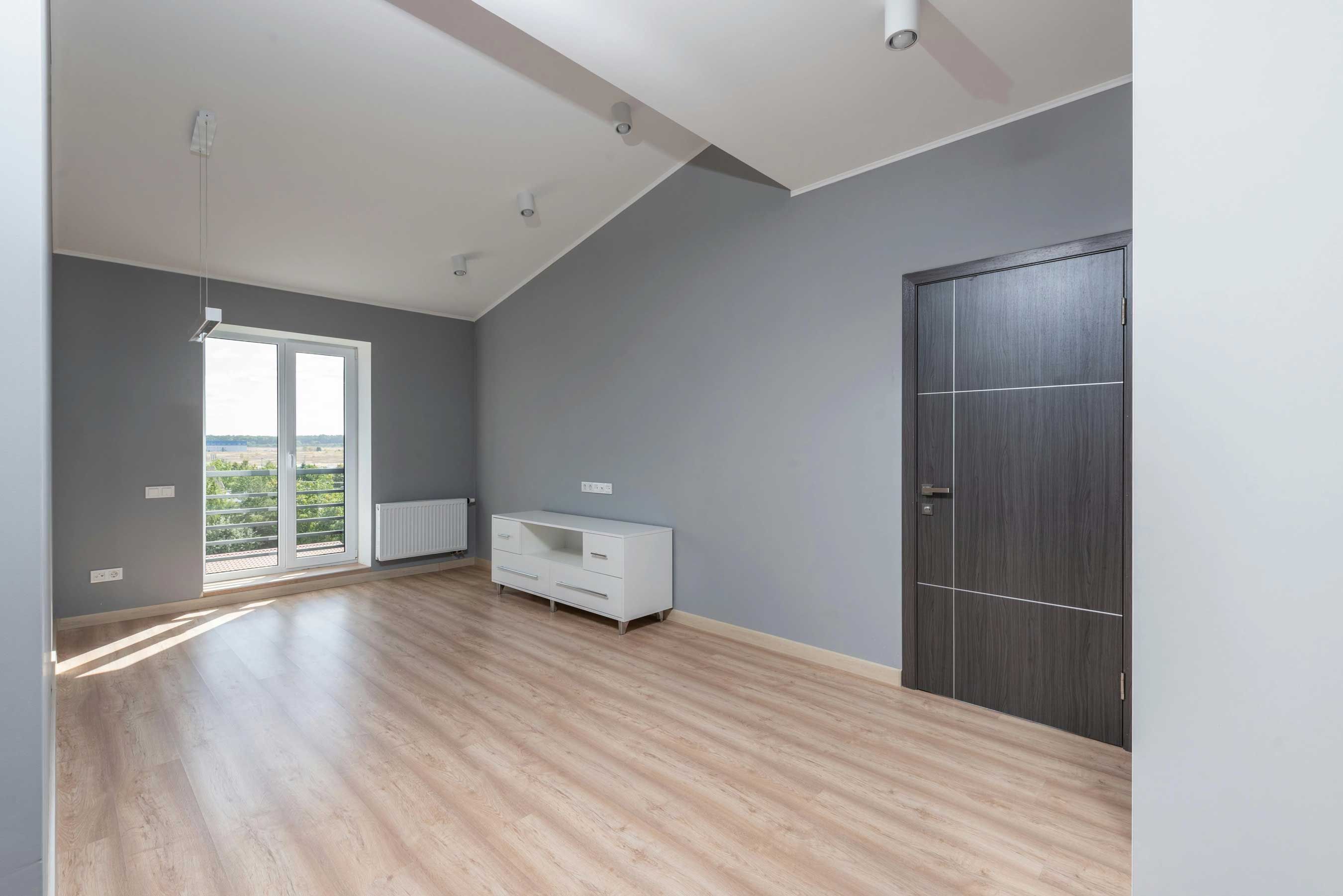 Salon rénové avec murs gris uniformes, plafond peint en blanc et parquet clair après travaux de peinture intérieure AK Rénovation.